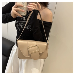 Close-up of beige shoulder bag with large gold buckle and adjustable strap on a model