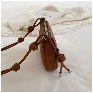 Detail of brown suede crossbody bag showing knotted strap and silver hardware on white fabric