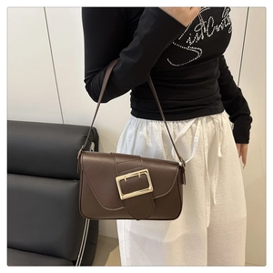 Détail d'un sac baguette en cuir marron foncé avec boucle dorée porté par un mannequin