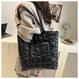 Close-up of a large black quilted tote bag with vertical stitching and metal ring detail