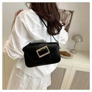 Detail of a black leather shoulder bag featuring a large decorative gold square buckle