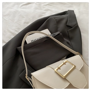 Détail d'un sac à bandoulière en cuir blanc crème avec une grande boucle en métal doré