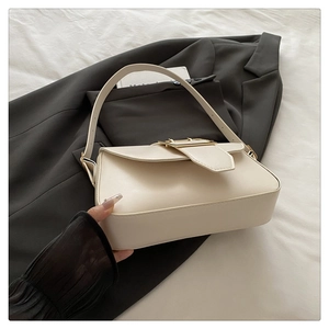 Gros plan d'un sac à main beige crème avec boucle dorée sur une veste de costume