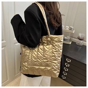 Detailed view of large quilted puffer tote bag in metallic gold worn by female model