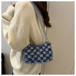 Detail of blue and white checkered denim baguette bag with fringe and gray strap on shoulder