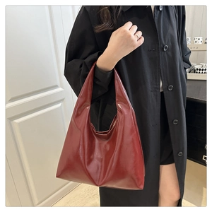 Détail d'un sac hobo en cuir verni rouge foncé porté avec un trench-coat noir élégant