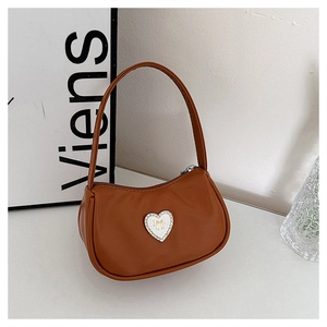 Detail of brown crescent shoulder bag with white heart and gold bow accent on white table