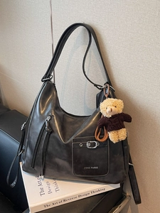 Versatile black leather tote bag with side zippers and a plush bear pendant charm