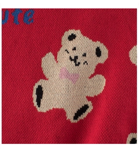 Detail shot of a red knitted sweater featuring a cream bear motif and blue embroidery