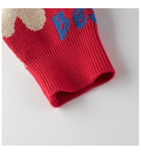 Detail of red knitted sweater cuff with ribbed texture and blue BE letter patterns