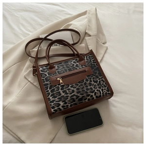 Detail of leopard print tote bag with brown leather handles and golden front zipper