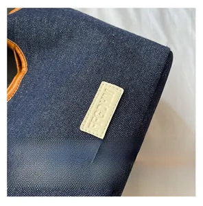 Detail der Denim-Einkaufstasche mit geprägtem Lederlogo und brauner Lederpaspelierung