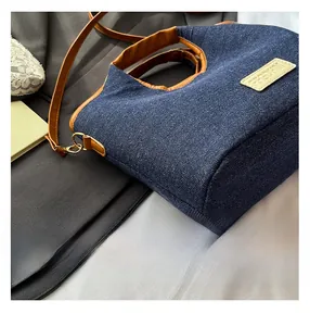 Detailansicht der dunkelblauen Denim-Beuteltasche mit braunem Ledergriff und Goldbeschlägen