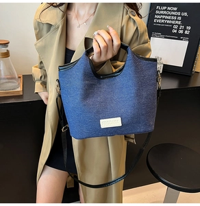 Detail der blauen Denim-Beuteltasche mit schwarzem Lederbesatz und Metallhaken am Trageriemen