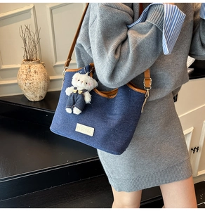 Detail of blue denim tote bag with brown leather trim and cute 3D plush bear charm