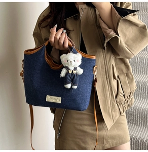 Detail of blue denim shoulder bag with brown leather trim and a plush bear pendant charm
