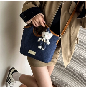 Detail of blue denim shoulder bag with brown leather trim and white plush bear charm