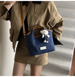 Detailed shot of a navy denim shoulder bag with brown leather trim and a plush bear charm