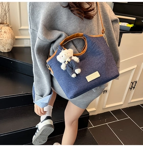 Detail of denim tote bag featuring a 3D teddy bear charm and brown leather trim accents