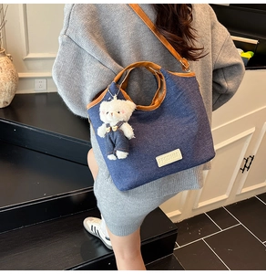 Detailed side view of denim tote bag featuring teddy bear charm and leather handles