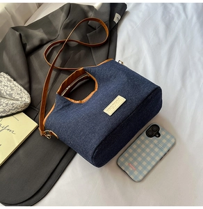 Detail view of denim tote bag with brown leather trim and bear patch on white linen
