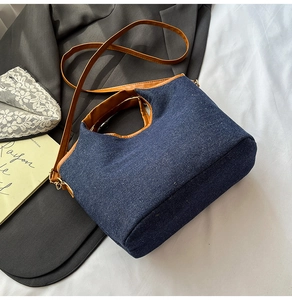 Detail of denim and brown leather handbag with gold hardware on minimalist background