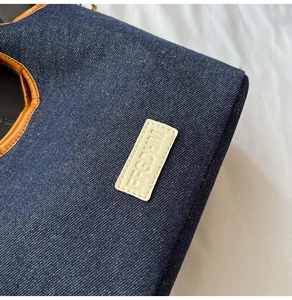 Detailed close-up of dark denim texture and brown leather trim on the bear handbag