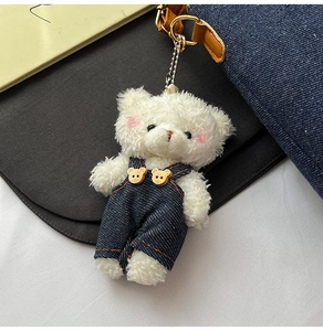 Detail of cute white plush bear charm wearing blue denim overalls with bear buttons