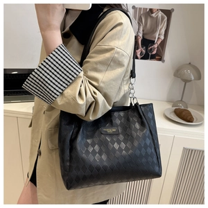 Close-up of black quilted tote bag with silver chain and gold logo label on shoulder