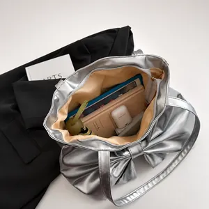 Metallic silver tote bag with large bow showing interior storage for iPad and daily items