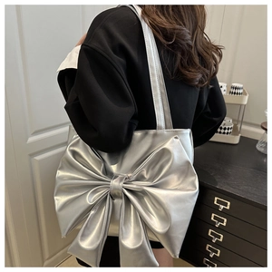 Silver metallic tote bag with large bow detail shown in a stylish lifestyle setting