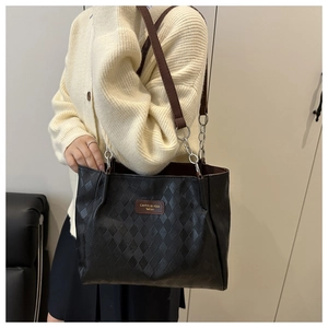 Detail of black tote bag with quilted texture, leather straps and silver chain accents