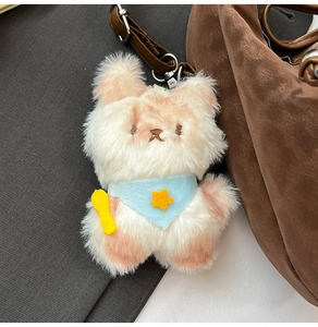 Close-up of a plush dog keychain with a blue bandana hanging on a stylish handbag