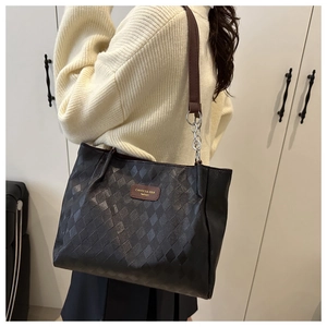 Detail of black quilted tote bag featuring a leather brand tag and metal chain strap
