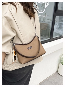 Detail of a brown dumpling crossbody bag with textured fabric and wooden bead charm