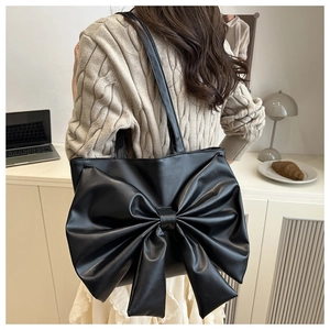 Detail of matte black tote bag with large bow decor worn by model in casual setting