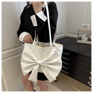 Close-up of white tote bag with oversized bow design worn by model in a minimal interior