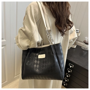 Close-up of black quilted leather tote bag with metal chain strap and logo plaque