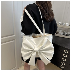 Detail of white large bow tote bag in PU leather worn over the shoulder by a model