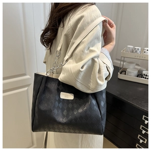 Detail of black quilted tote bag with chain strap and logo patch on model's shoulder