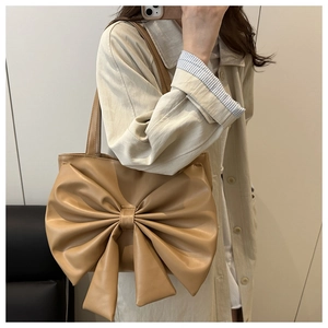 Fashionable oversized bow-knot tote bag in beige PU leather worn on shoulder by model