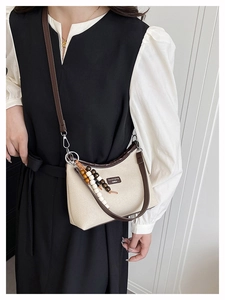 Detail of canvas crossbody bag with dark brown leather trim and wooden bead tassel ornament