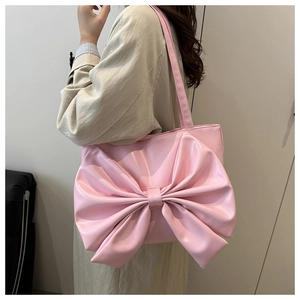 Detailed view of pink tote bag with oversized bow and long shoulder strap worn by model