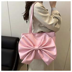 Close-up of pink faux leather tote bag featuring a large bow and thin shoulder strap