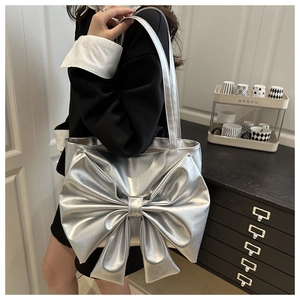 Detail of silver metallic tote bag featuring a large bow design worn over the shoulder