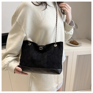 Détail d'un sac à bandoulière matelassé noir avec chaîne porté par un mannequin en scène