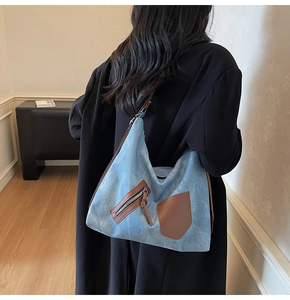Side view of large blue denim Hobo bag with brown leather accents and slim shoulder strap