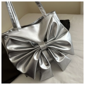 Close-up of metallic silver tote bag featuring a large bow detail and high-gloss finish