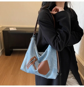 Detail of blue denim tote bag featuring brown leather straps and front zipper pocket
