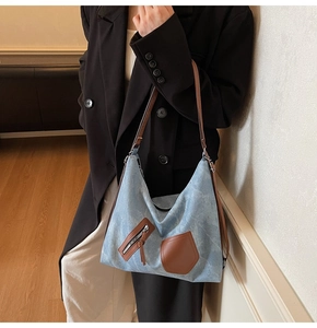 Fashionable blue denim tote bag with brown leather details worn by a model in a suit